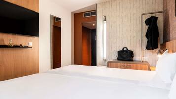 A hotel room with a large bed, a TV mounted on the wall, a wooden dresser, and a mirror with a hanging robe.
