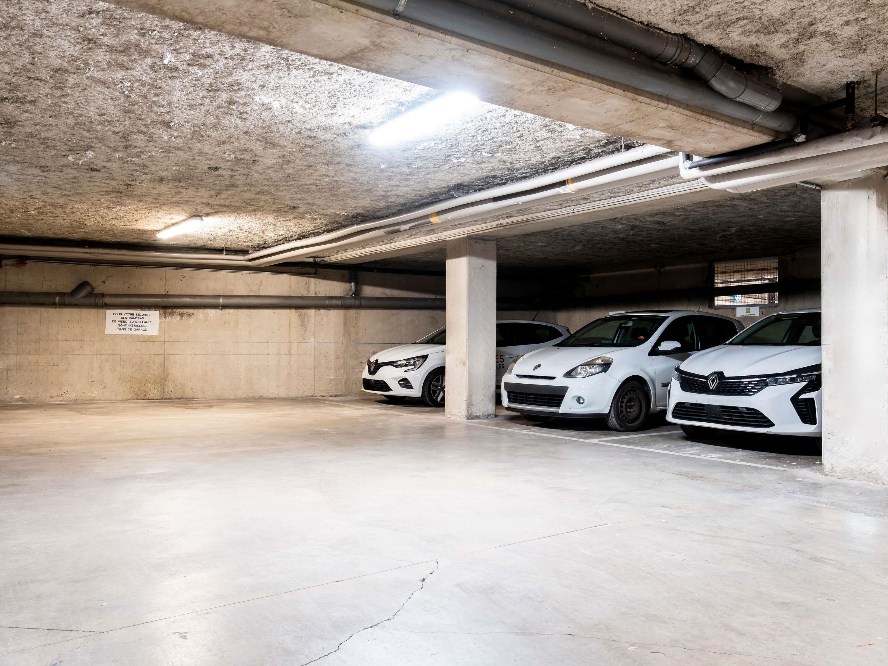 A parking garage with concrete pillars, overhead pipes, and a sign in French.