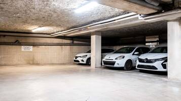 A parking garage with concrete pillars, overhead pipes, and a sign in French.