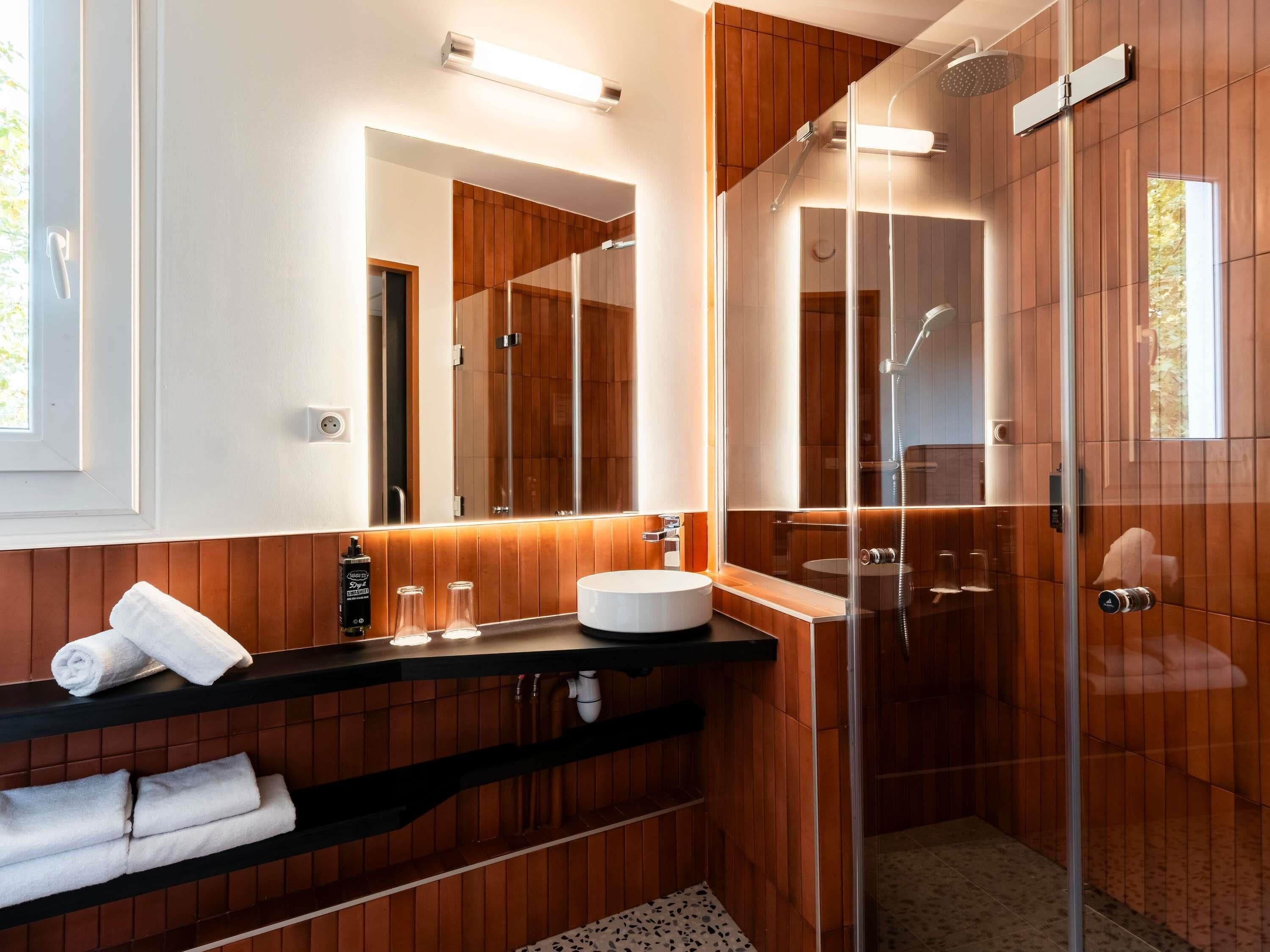 Un baño moderno con ducha envuelta en vidrio, tocador con lavamanos y espejo.