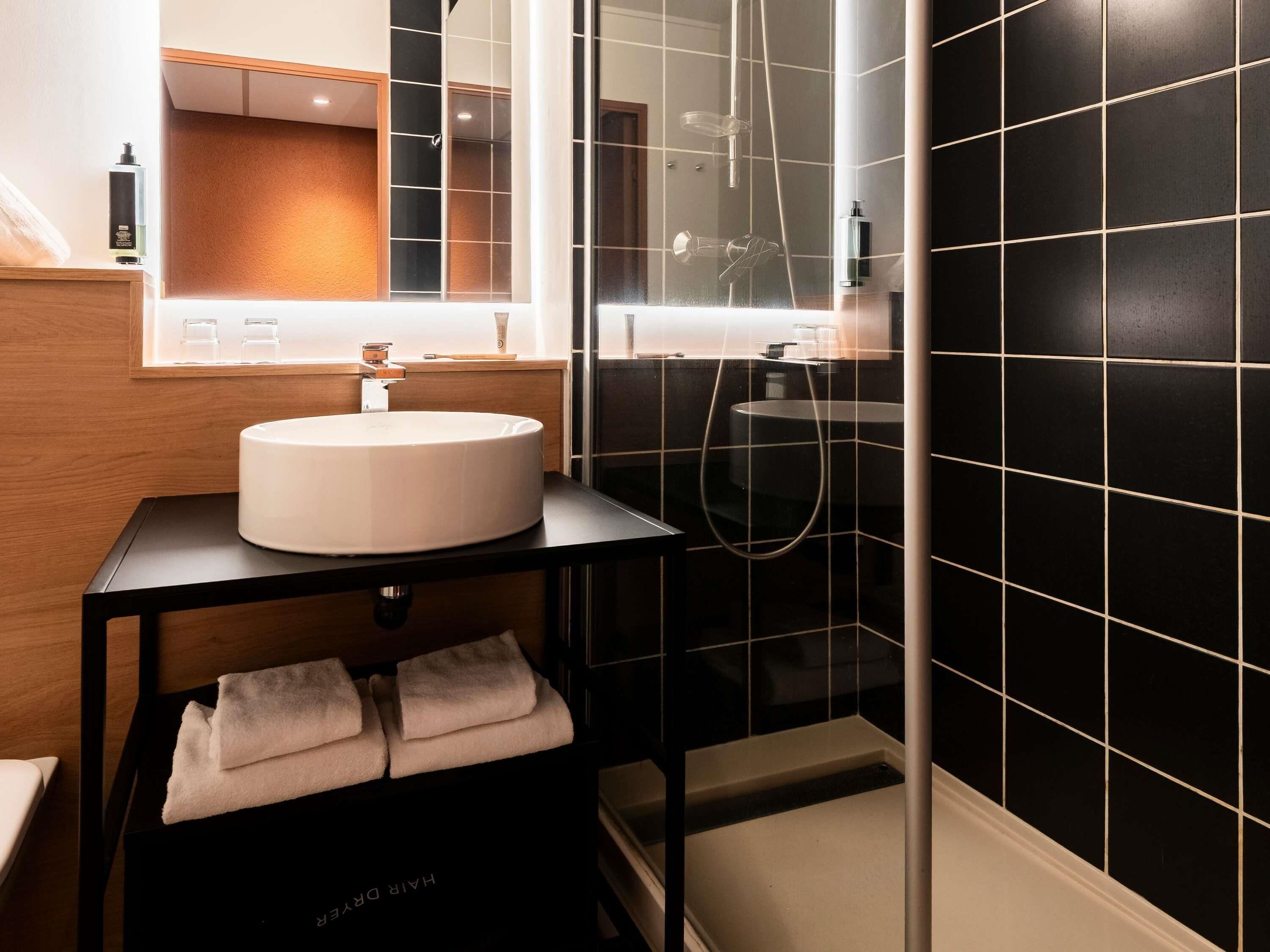 A modern bathroom with a round sink, a mirror, a glass shower enclosure, and a towel rack.