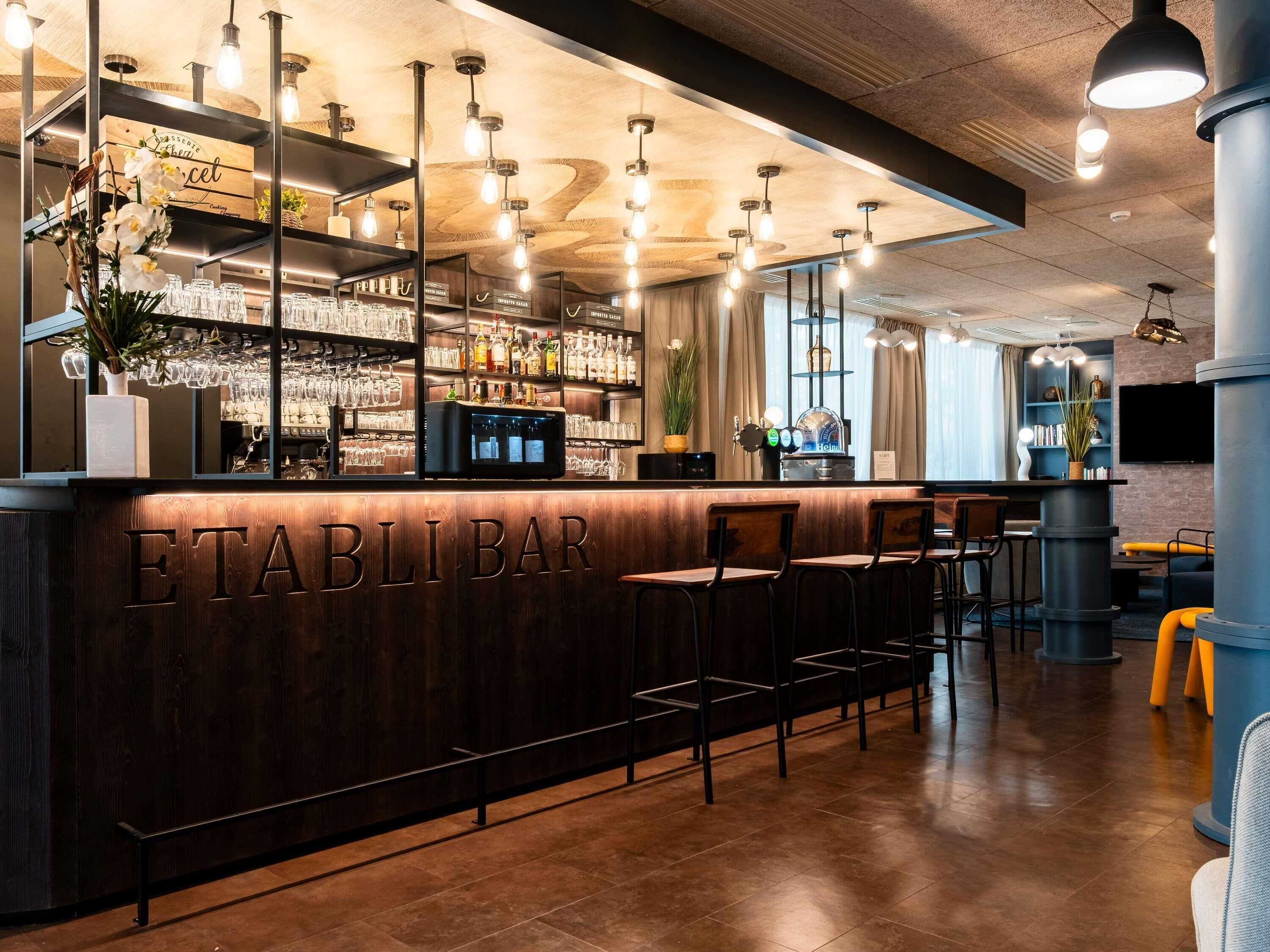 A bar area with a wooden counter, bar stools, and a digital screen.