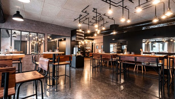 A modern cafe interior with exposed ductwork, wooden tables, and bar stools.