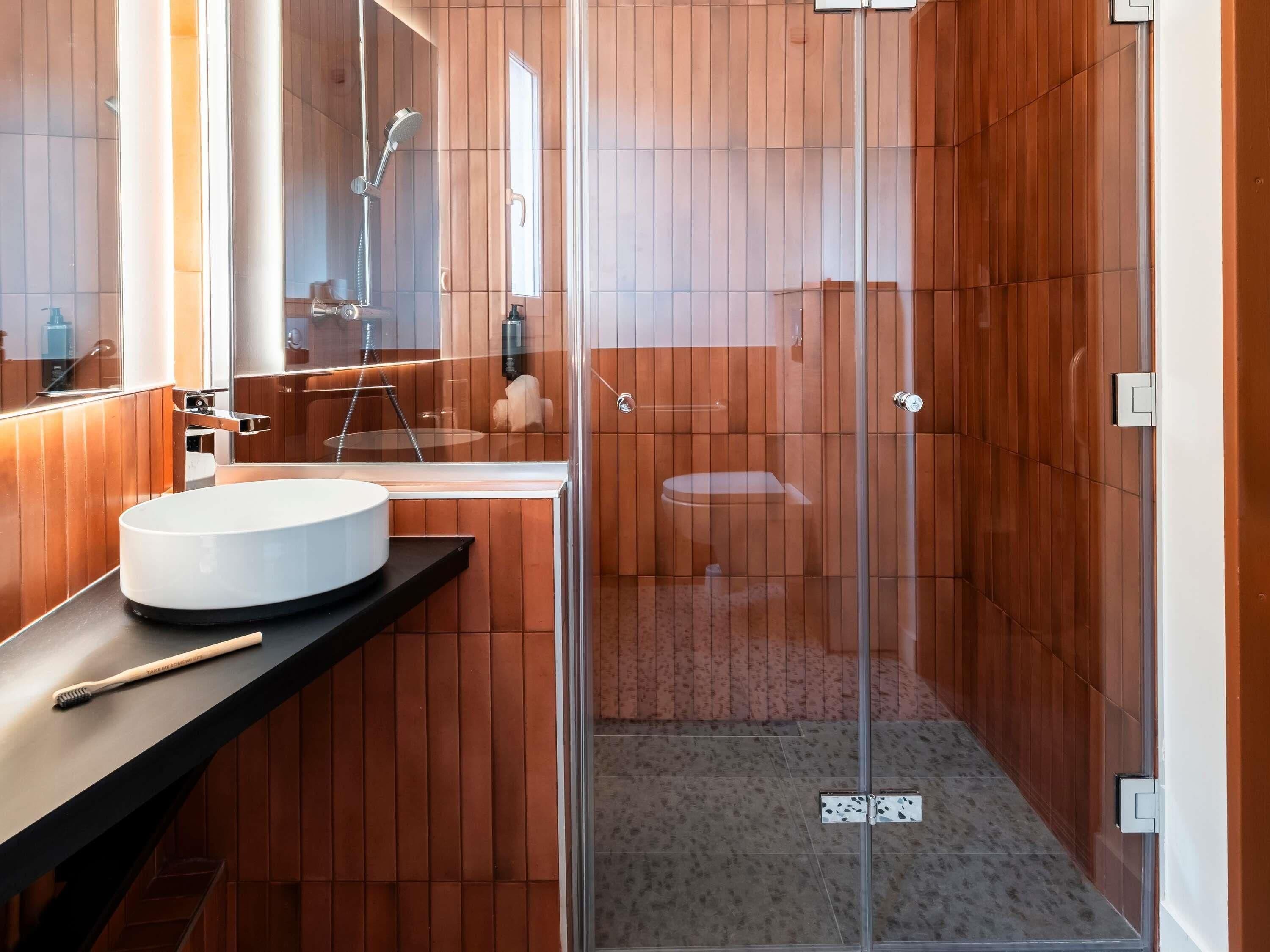 A modern bathroom with a round sink, a glass shower enclosure, and wooden paneling.