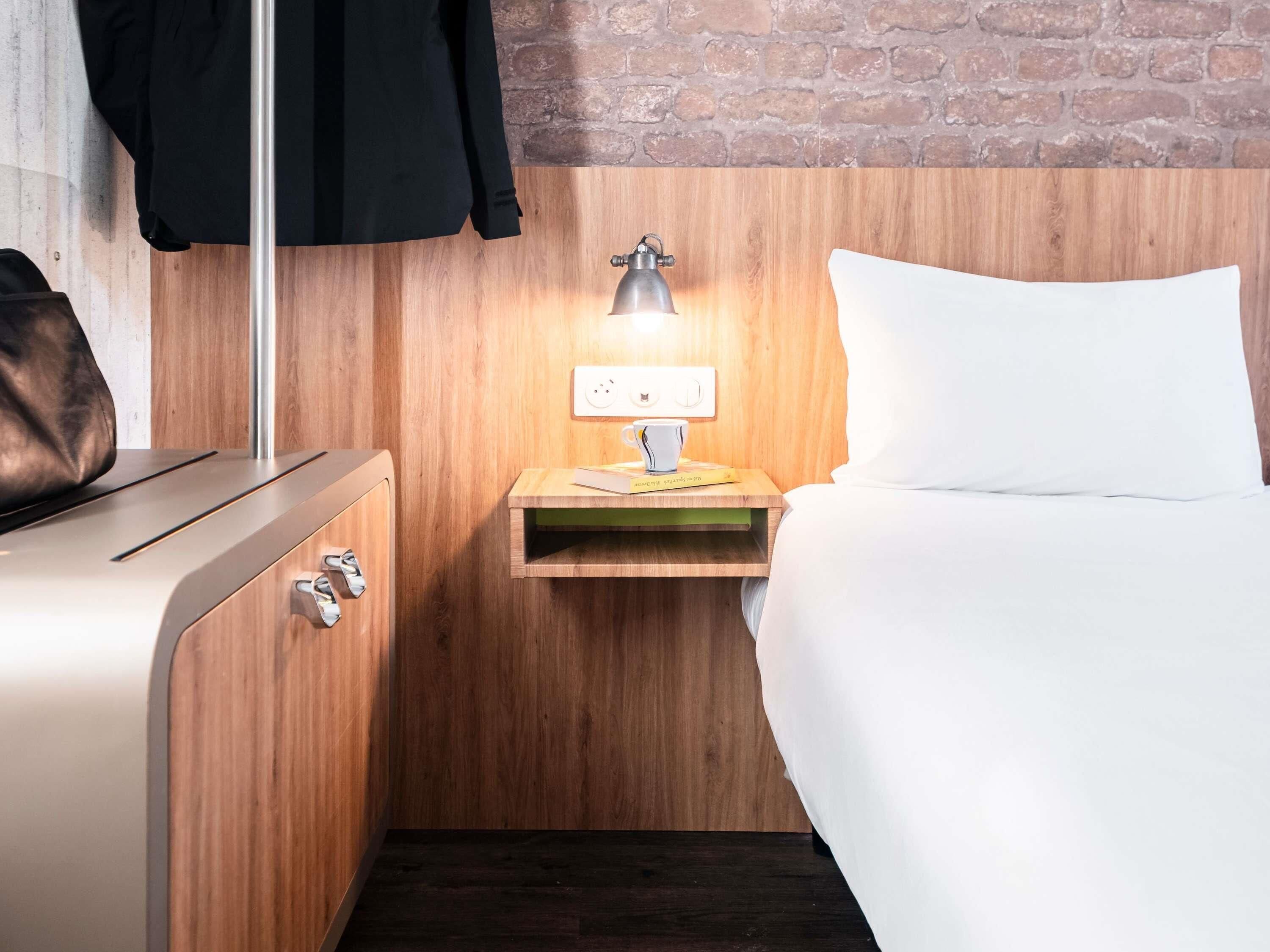 A hotel room with a wooden wall, a bedside table with a lamp, a bed, and a suitcase.