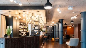 A modern bar area with a wooden reception desk, multiple hanging pendant lights, and a seating area with chairs and tables.