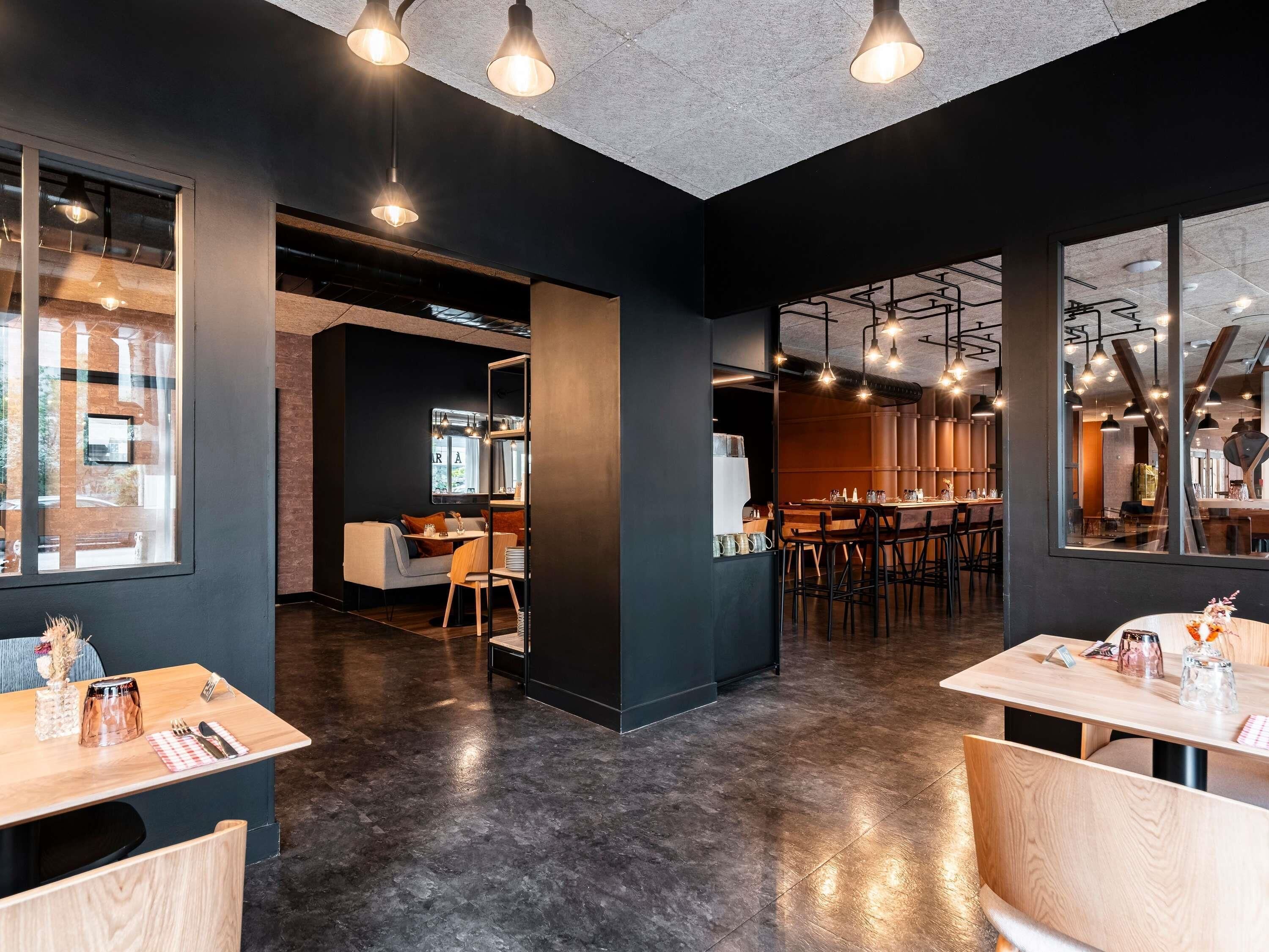 A modern interior with dark walls, wooden tables, and hanging pendant lights.