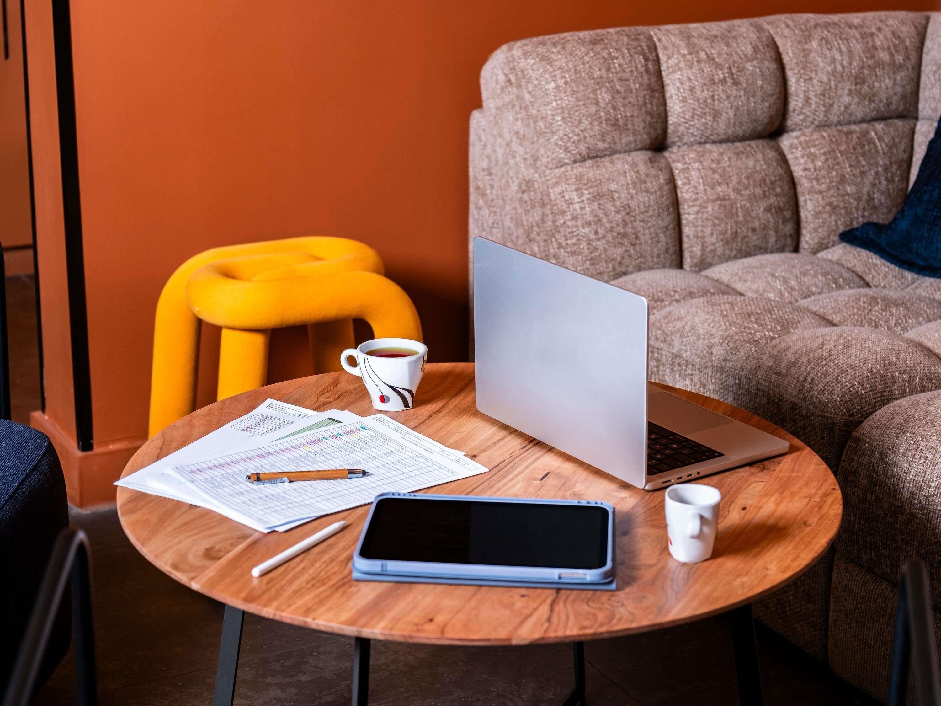 Una mesa de madera redonda con una computadora portátil, un teléfono inteligente, una taza y documentos.