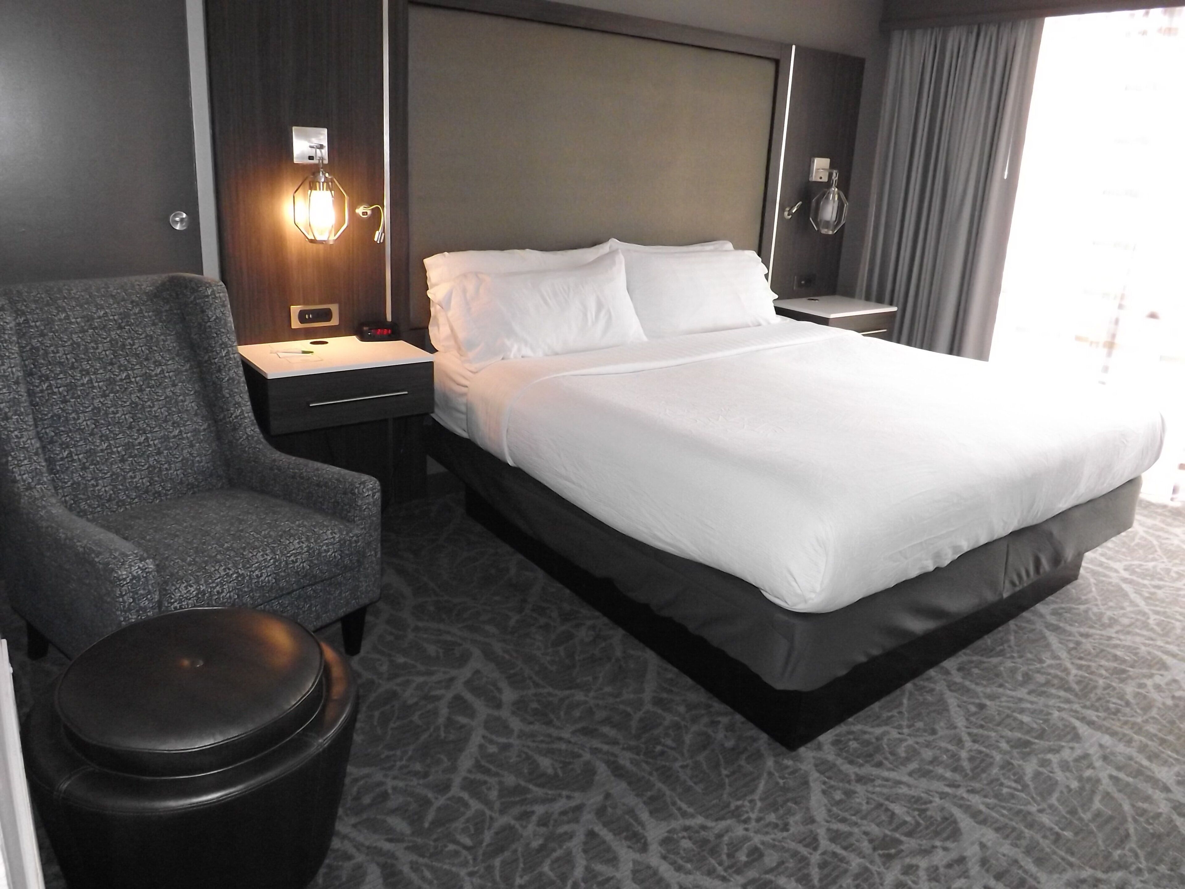 Une chambre d’hôtel avec un lit, une chaise, une table de chevet et une lampe.
