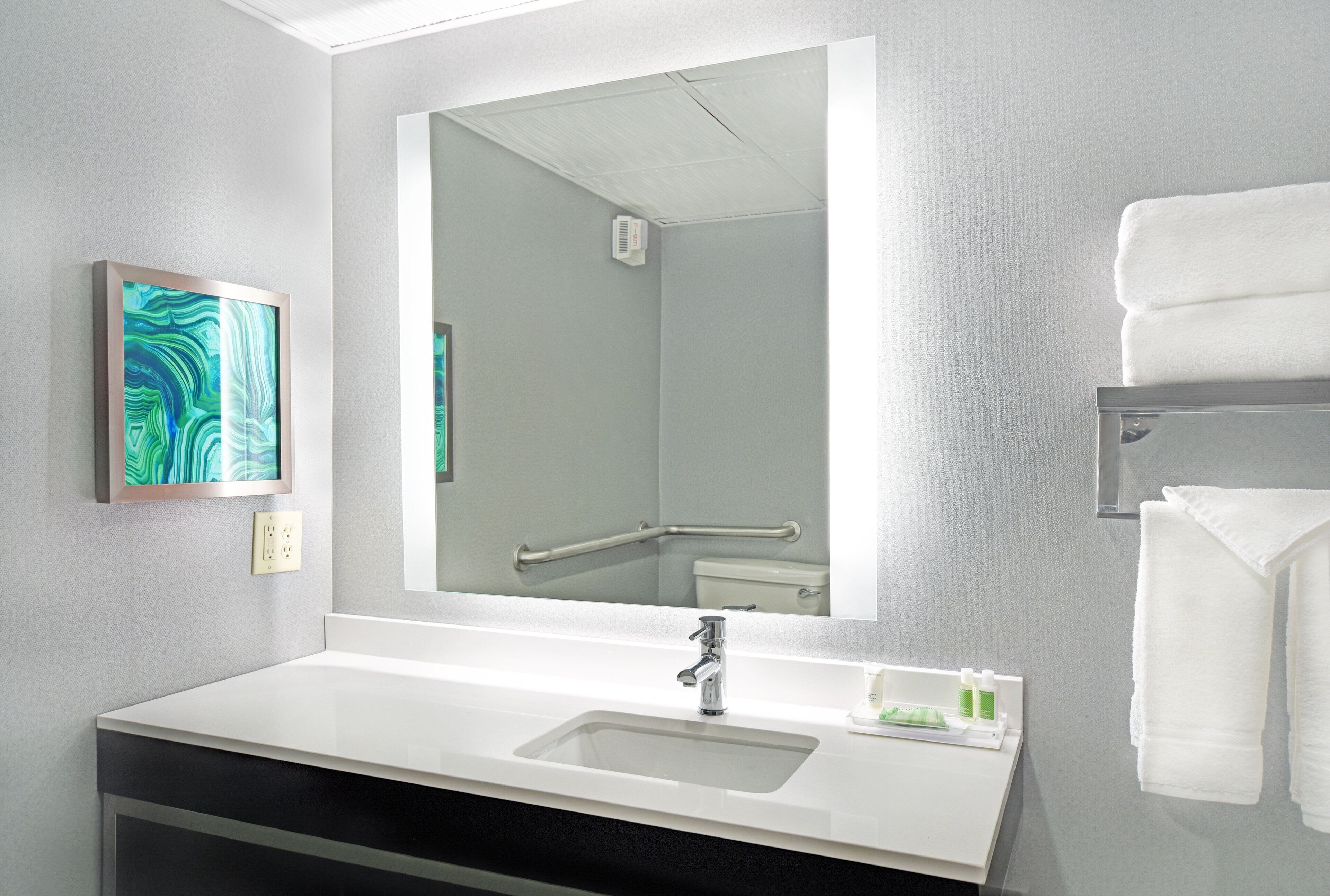 Un baño moderno con un lavabo blanco, un espejo grande y un perchero para toallas.