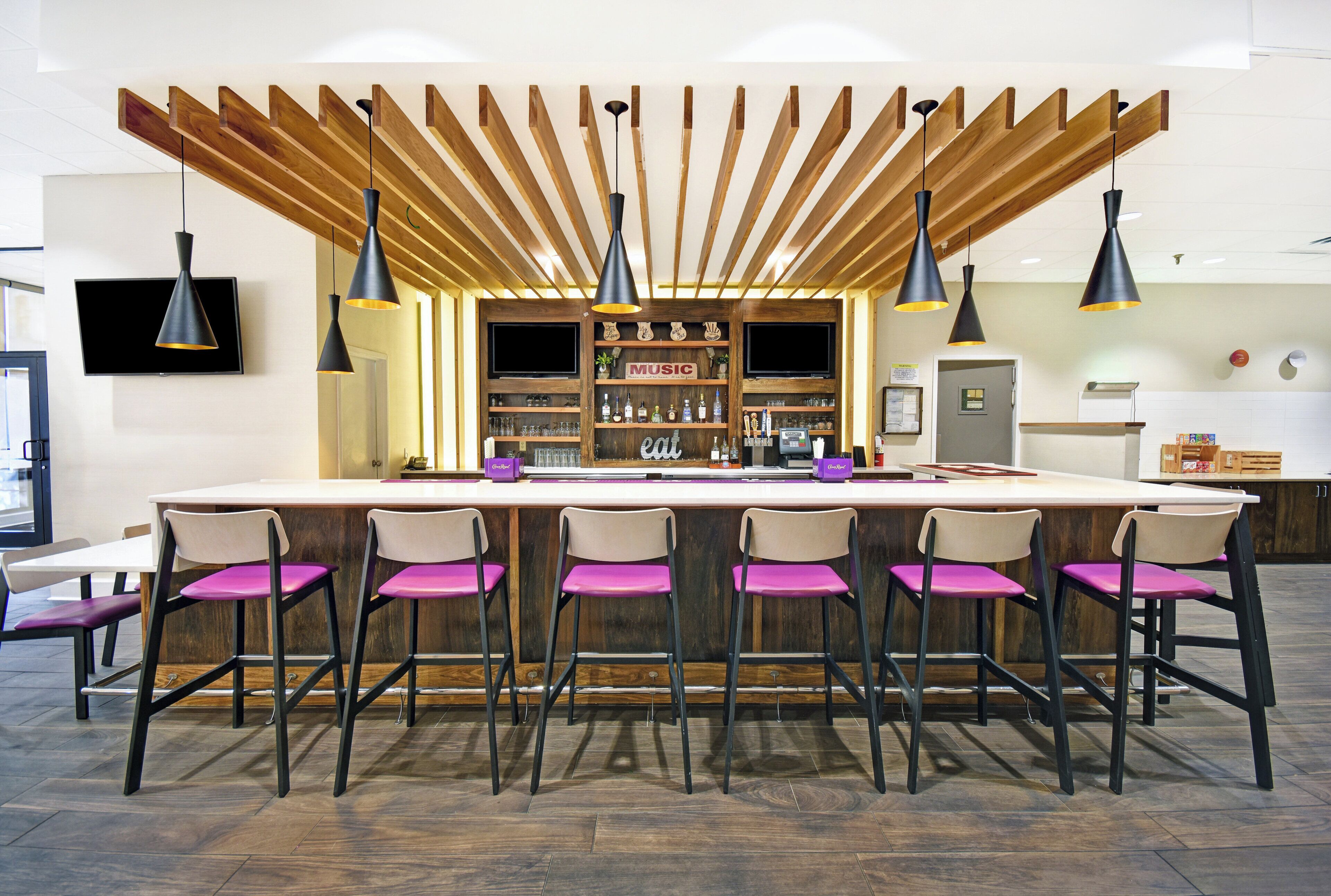 A bar area with wooden beams, black pendant lighting, and bar stools with purple cushions.