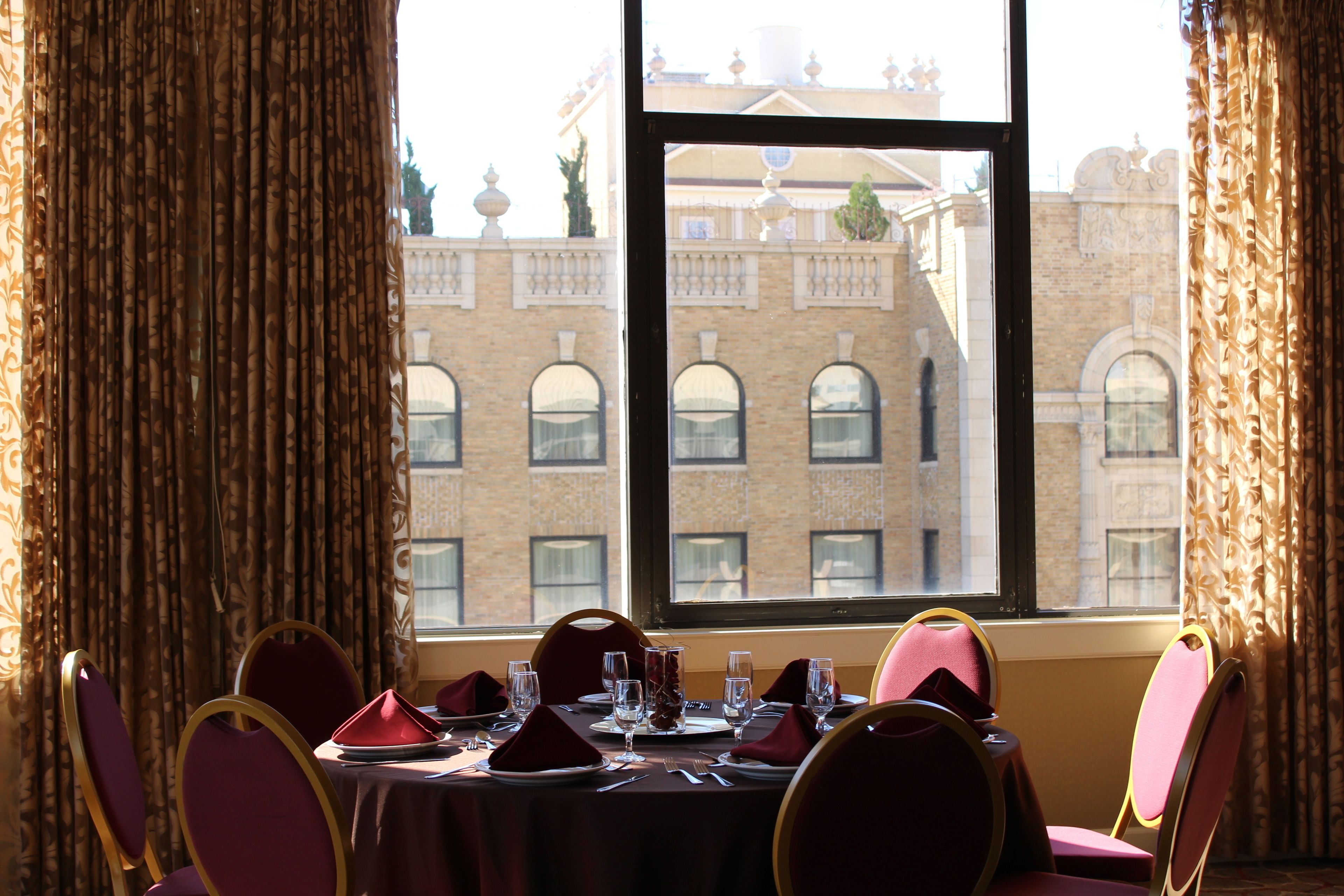 A dining area with a table set for four, a view of a building through a window, and curtains on either side.