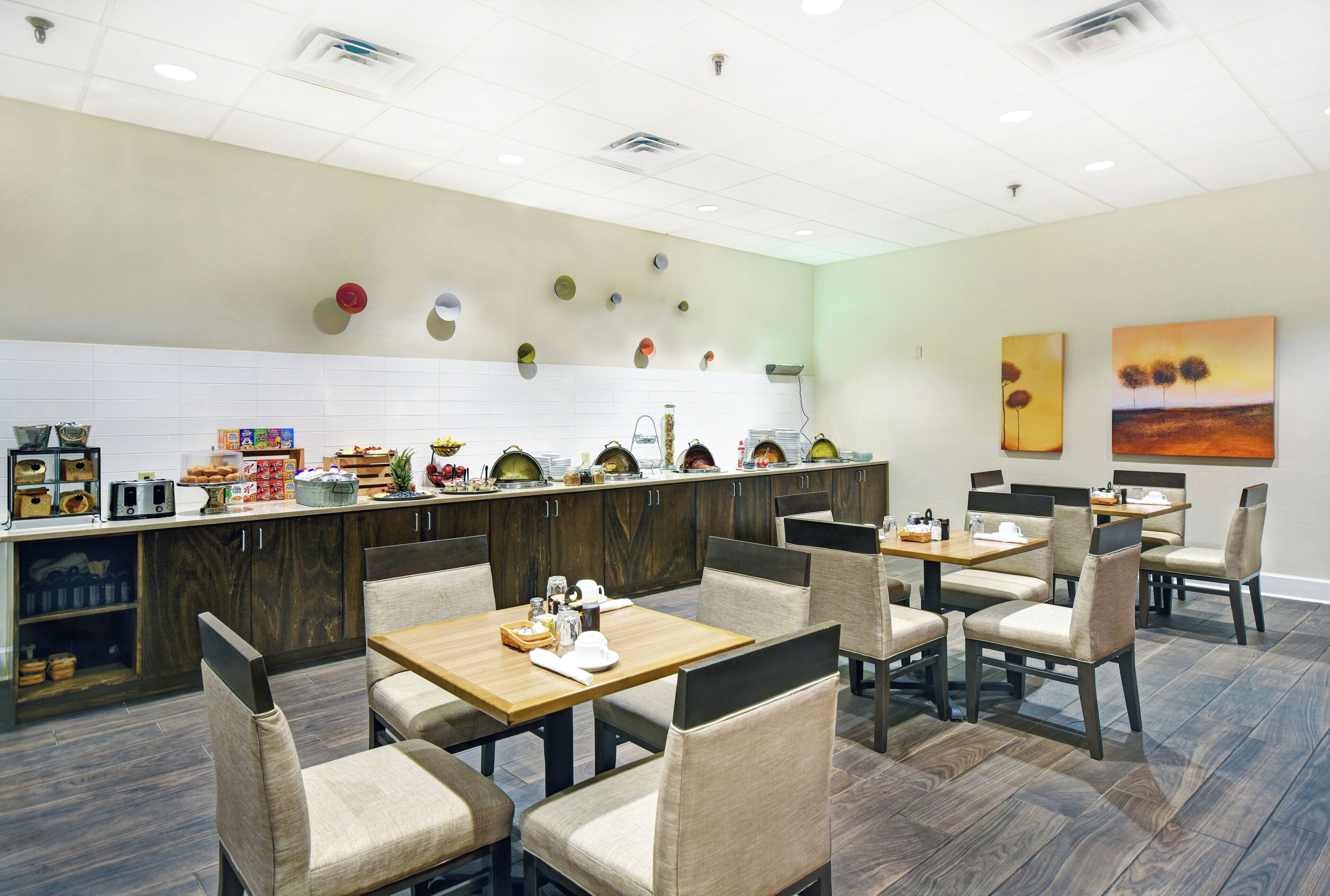 A restaurant with multiple dining tables and chairs, a counter with food items, and wall art.