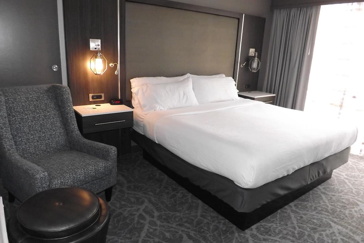 Habitación de hotel con una cama grande, una silla, una mesita de noche y una lámpara.