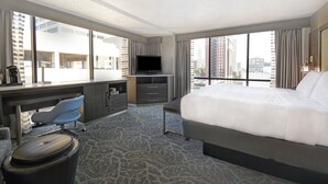 A hotel room with a large bed, a desk with a chair, a television, and a view of the city through large windows. - Holiday Inn Downtown Memphis by IHG (Memphis)