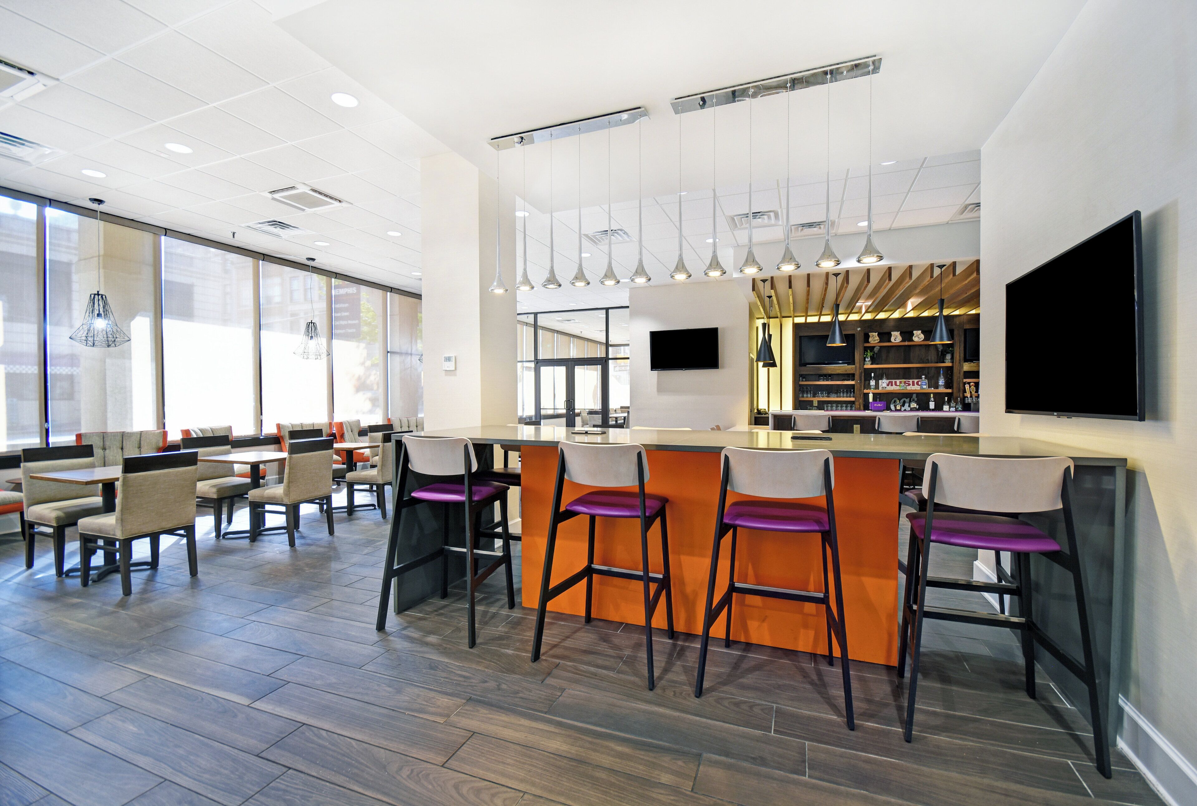 A modern bar area with high stools, a flat-screen TV, and pendant lighting.