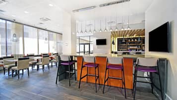 A modern bar area with high stools, a flat-screen TV, and pendant lighting.
