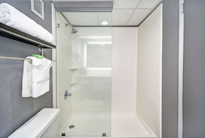 A modern bathroom with a glass-enclosed shower, a white bathtub, and a towel rack with folded towels.