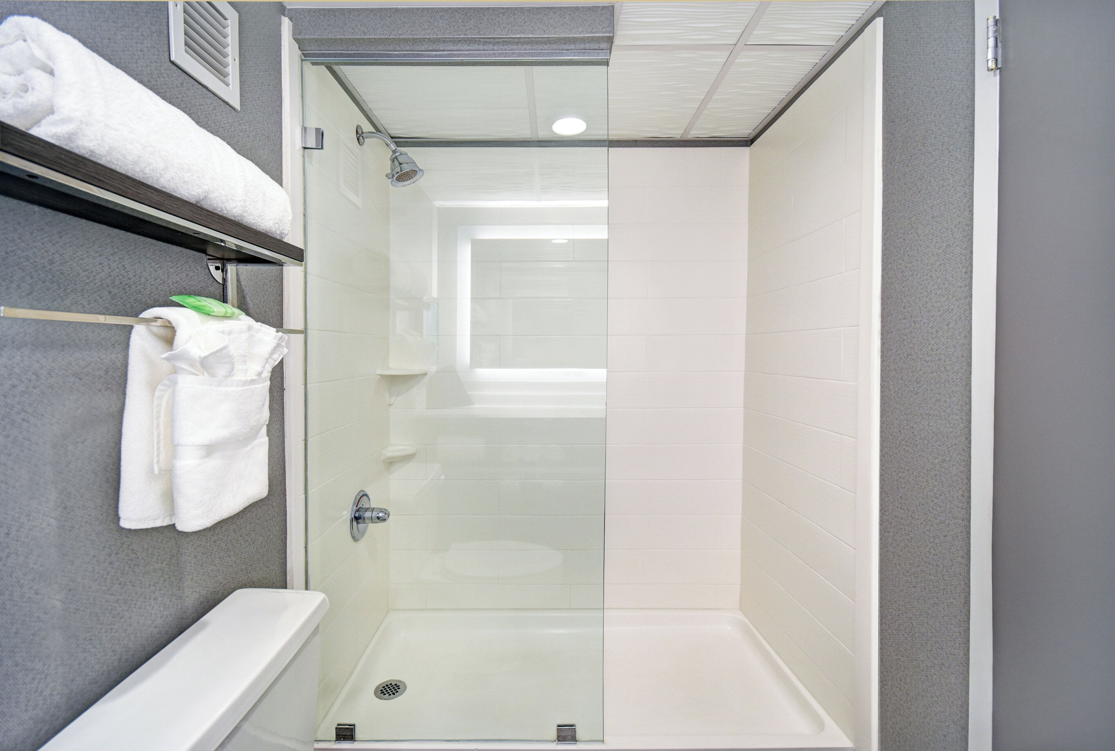 A modern bathroom with a glass-enclosed shower, a white bathtub, and a towel rack with towels.