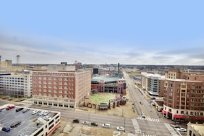 A cityscape with a multi-story parking garage, a large building with a distinctive red and white facade, and a spacious plaza with a colorful mosaic.