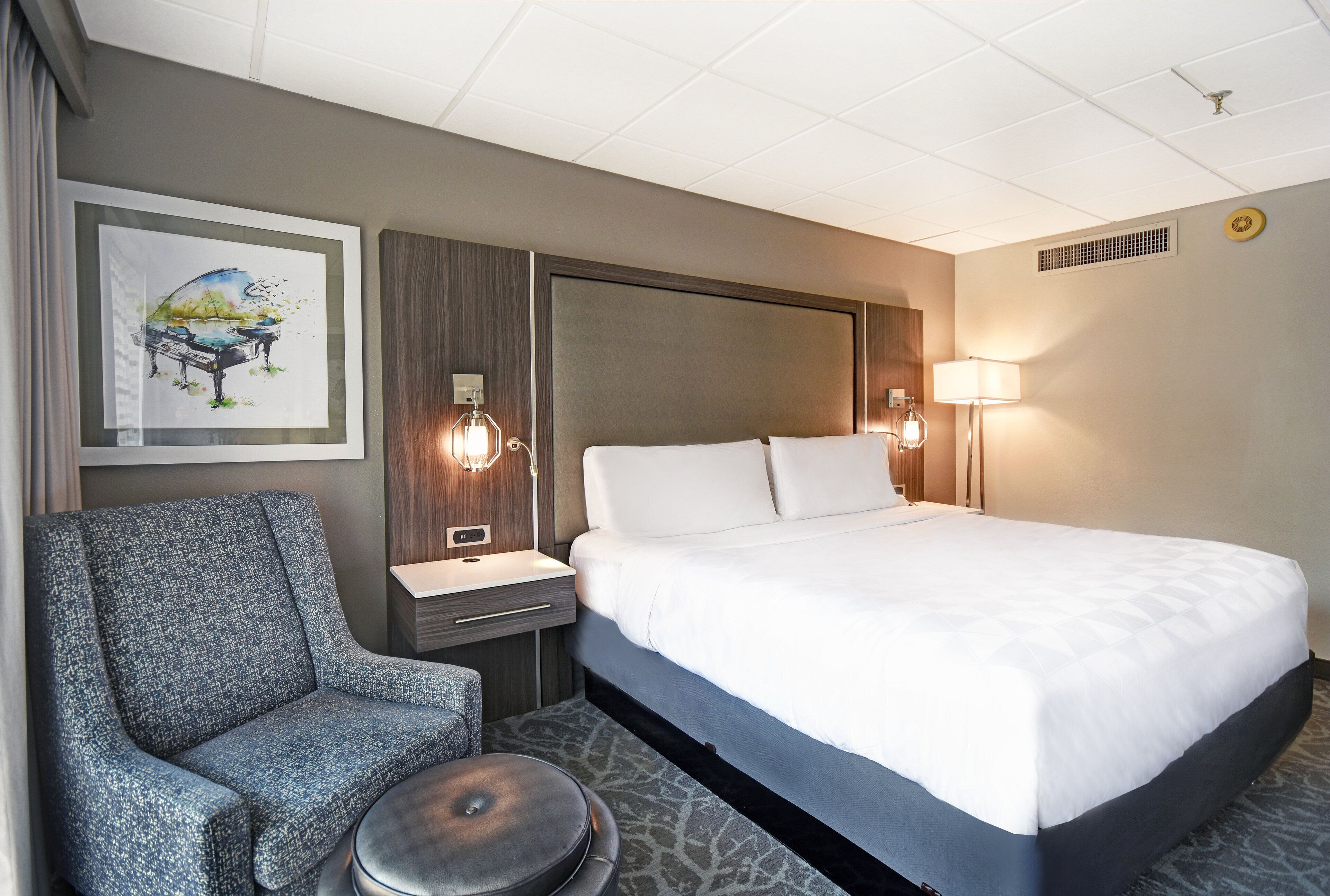 Ein Hotelzimmer mit einem großen Bett, einem Sessel, einem kleinen Tisch und einem Bild an der Wand.