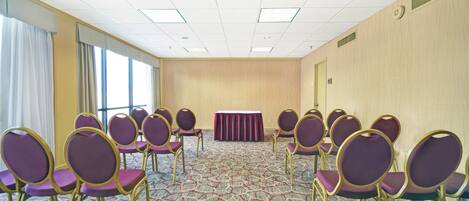 Sala de conferências com fileiras de cadeiras roxas, piso coberto de carpete e uma grande janela em um dos lados.