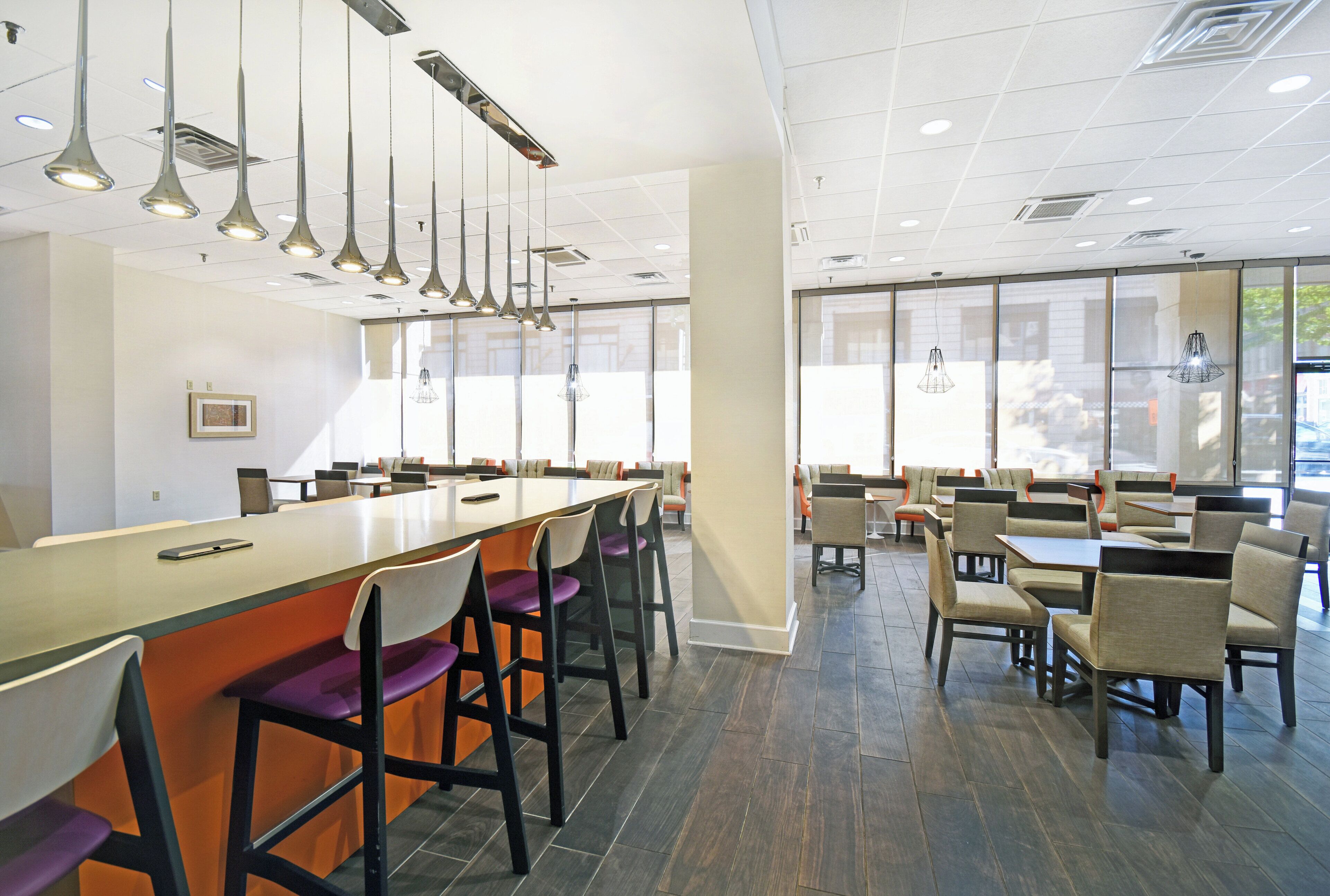 Ein modernes Restaurant-Interieur mit hohen Tischen, Stühlen und Pendelleuchten.