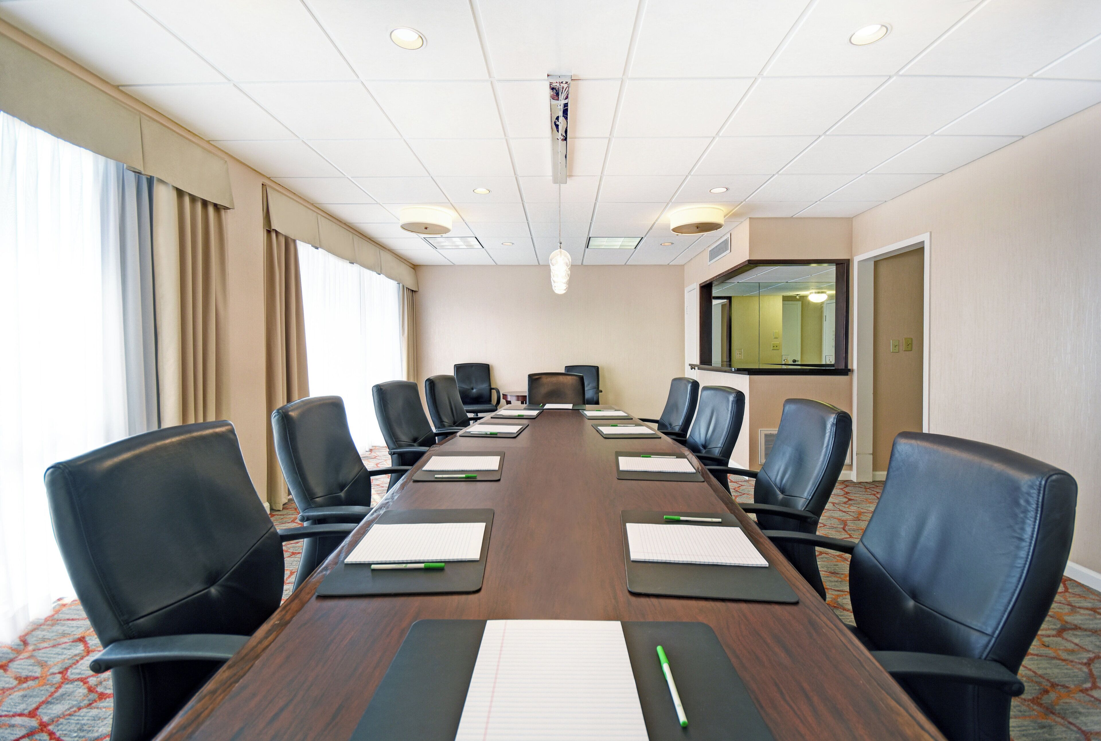 A conference room with a long table, black chairs, and a large mirror on the wall.