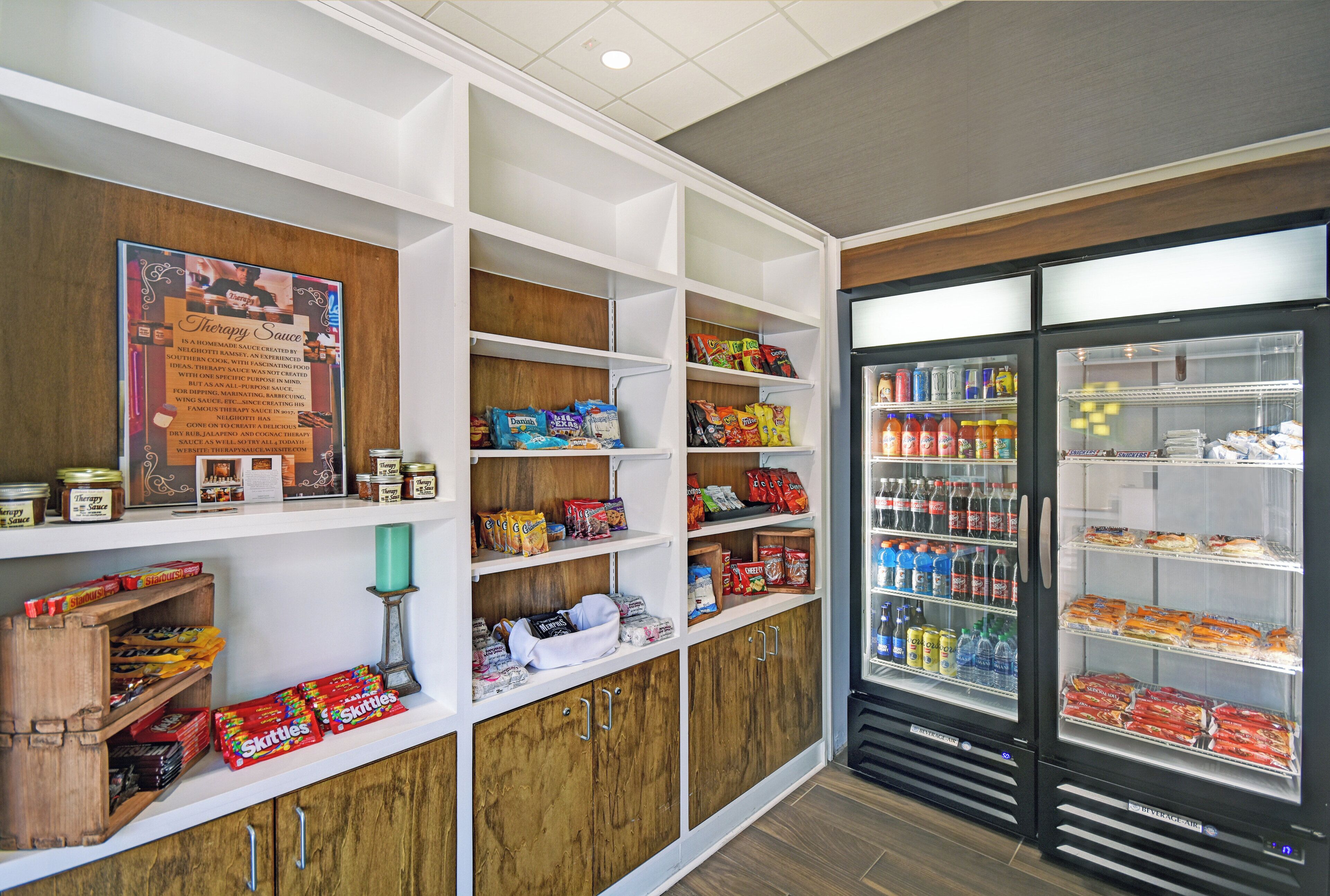 A snack bar with shelves stocked with various snacks, a refrigerator with beverages, and a poster on the wall.