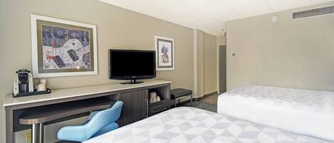 A hotel room with a bed, a desk with a television, and two framed pictures on the wall.
