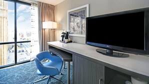 A hotel room with a large window, a desk with a flat-screen TV, a blue chair, and a coffee maker. - Holiday Inn Downtown Memphis by IHG (Memphis)
