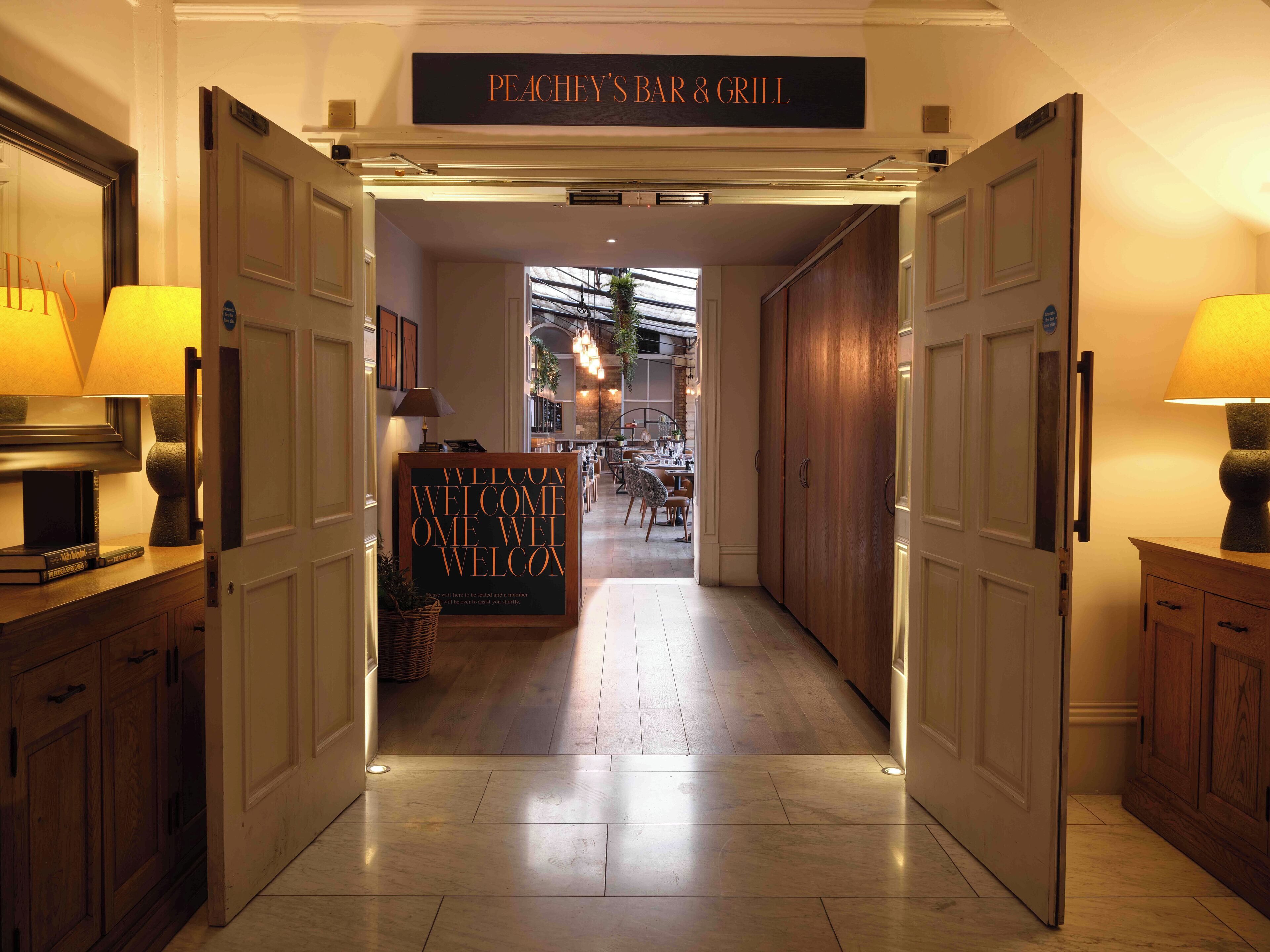 Un vestíbulo de hotel con un letrero que dice "PEACHEY'S BAR & GRILL" y una señal de bienvenida.