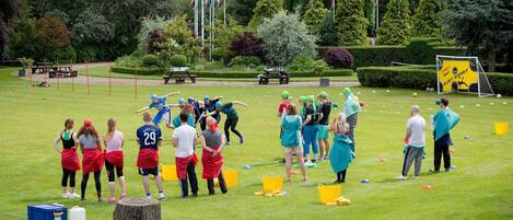 A group of people playing a game on a grassy field with a goalpost and flags in the background.