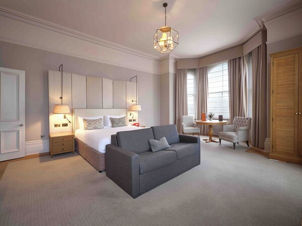 A hotel room with a large bed, a grey sofa, a round coffee table, and a wooden wardrobe.