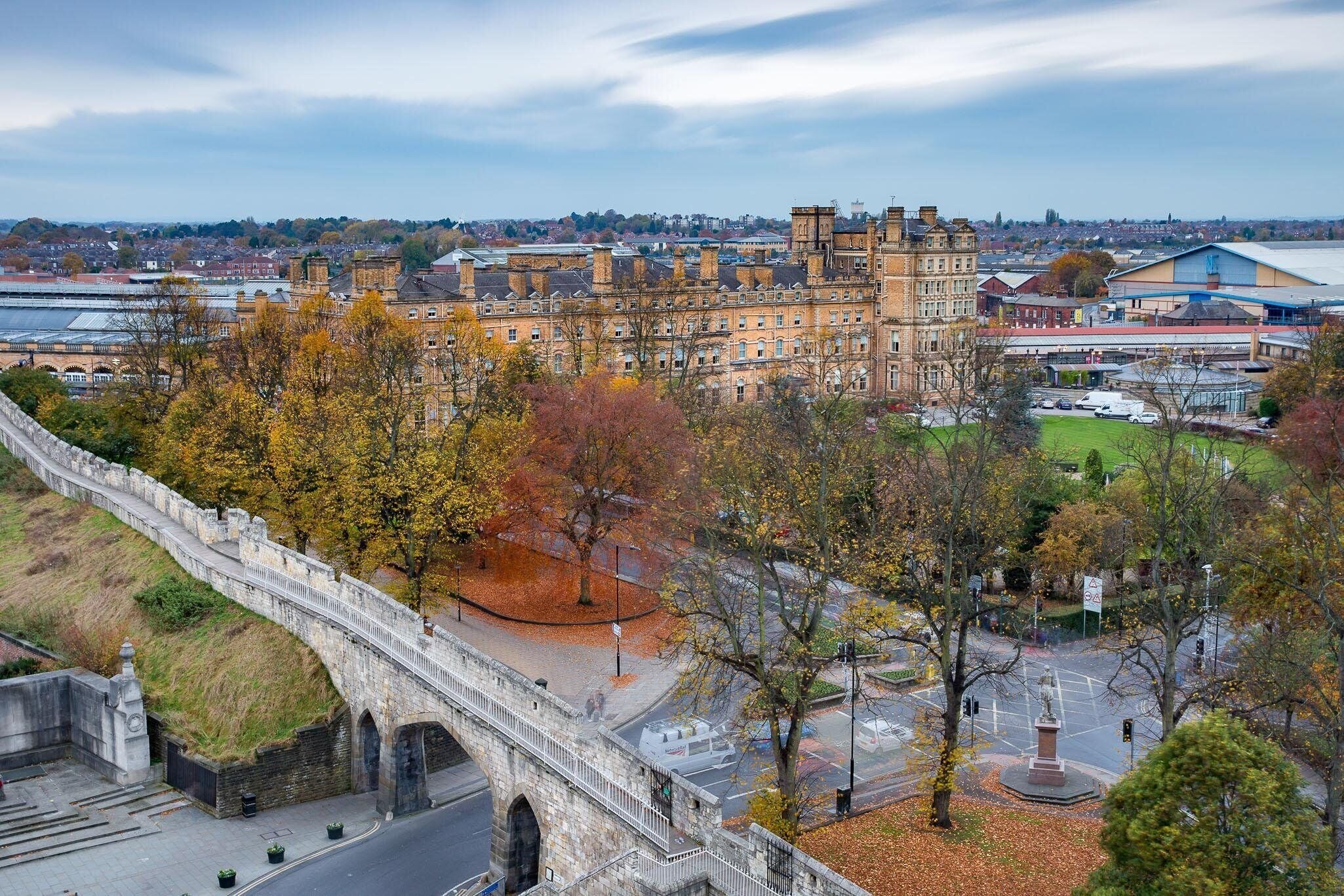 A historic stone bridge, a large building with multiple stories, and a park area with trees.