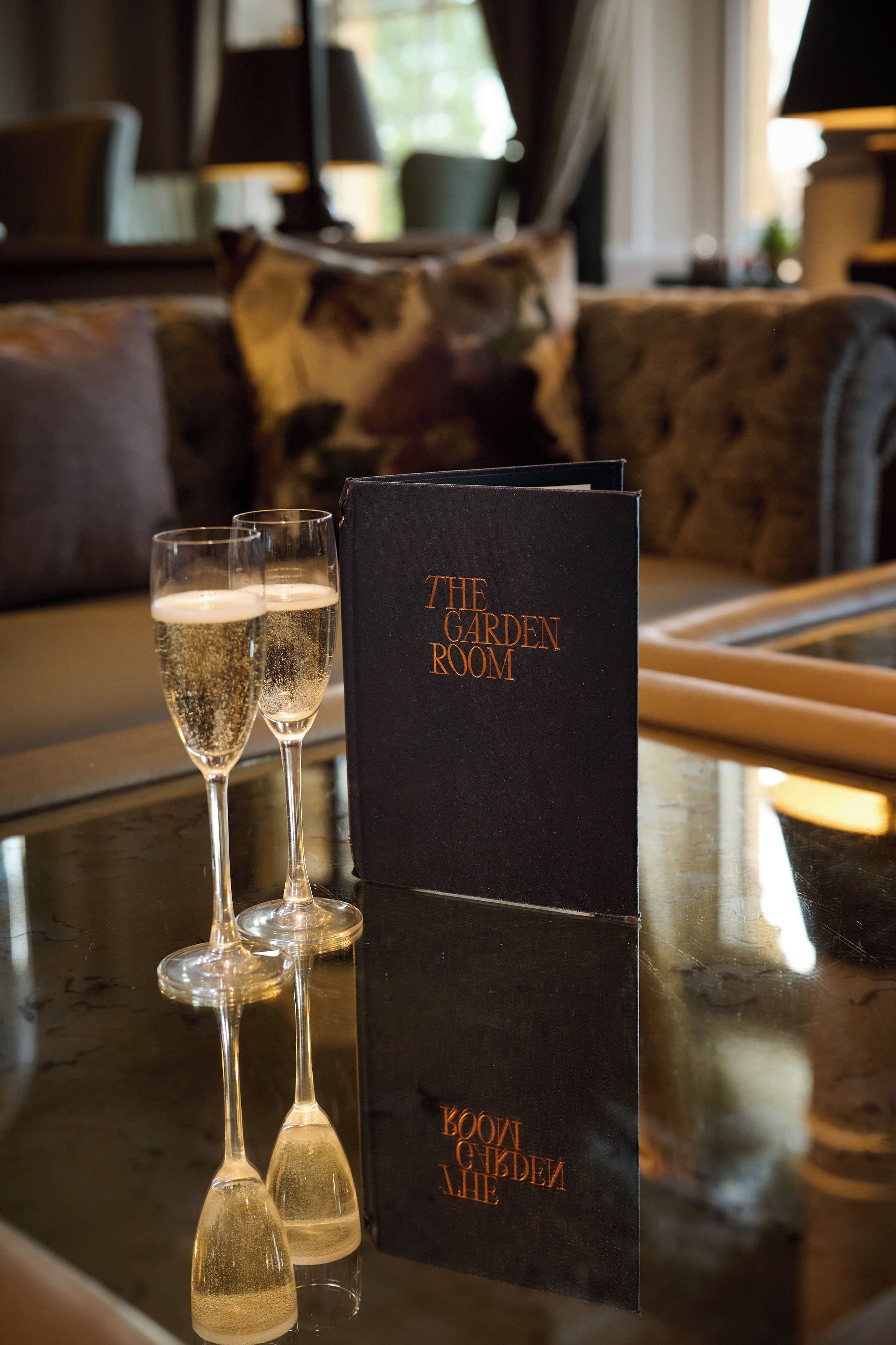 A black book titled "THE GARDEN ROOM" on a glass table with two champagne flutes.