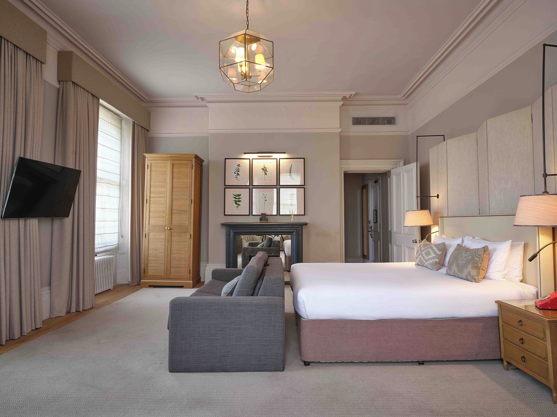 A hotel room with a large bed, a sofa, a TV, a fireplace, and a wardrobe.