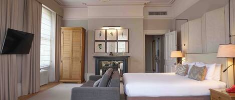A hotel room with a large bed, a sofa, a TV, a fireplace, and a wardrobe.