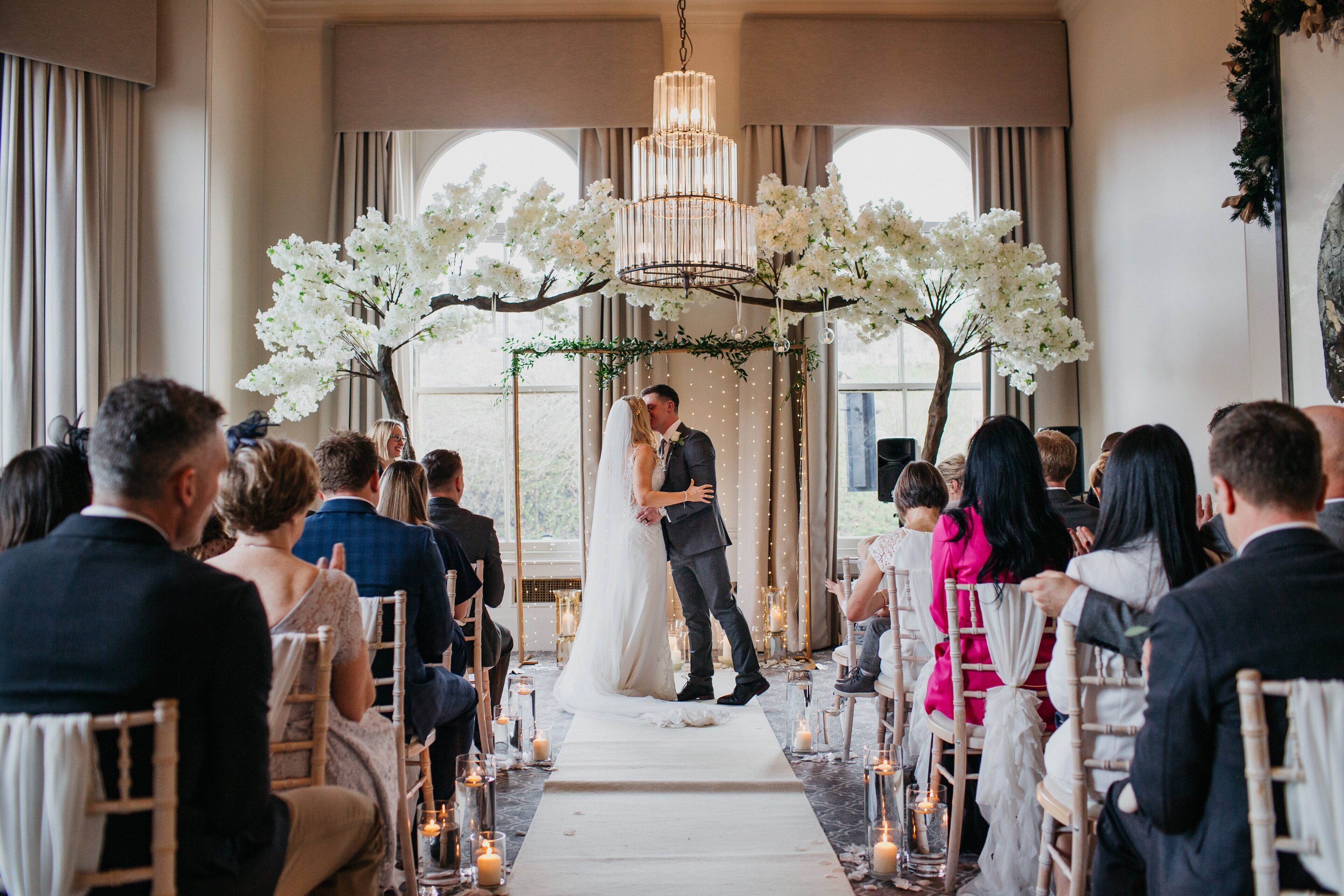 A wedding ceremony with a bride and groom at the altar, surrounded by guests seated on chairs.