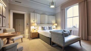 Ein modernes Hotelzimmer mit einem großen Bett, einer Sitzecke mit Tisch und Stühlen, einem Schreibtisch und einem großen Fenster mit Vorhängen.