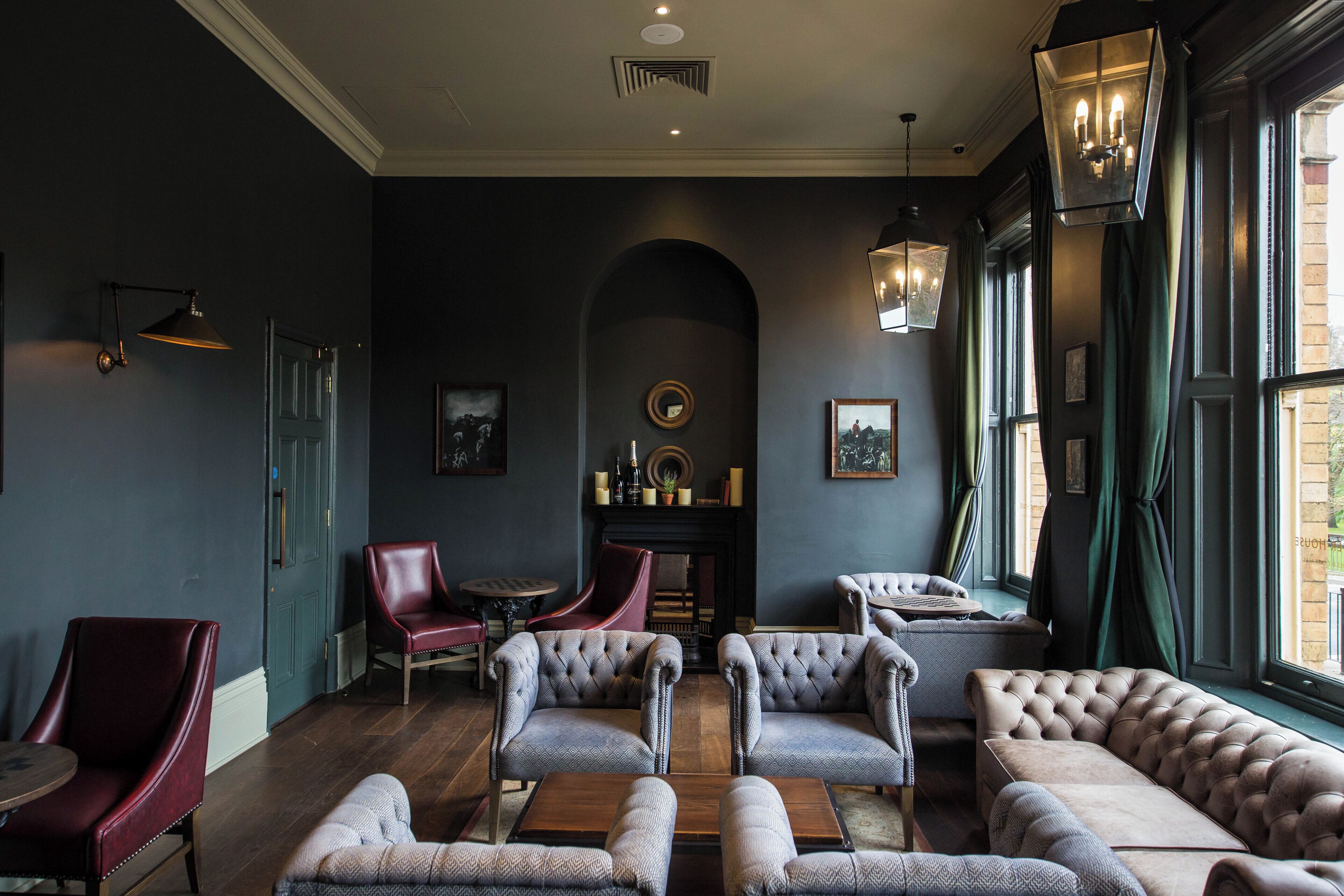 A dark-themed lounge with leather sofas, armchairs, and a fireplace.