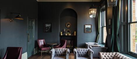 A dark-themed lounge with leather sofas, armchairs, and a fireplace.