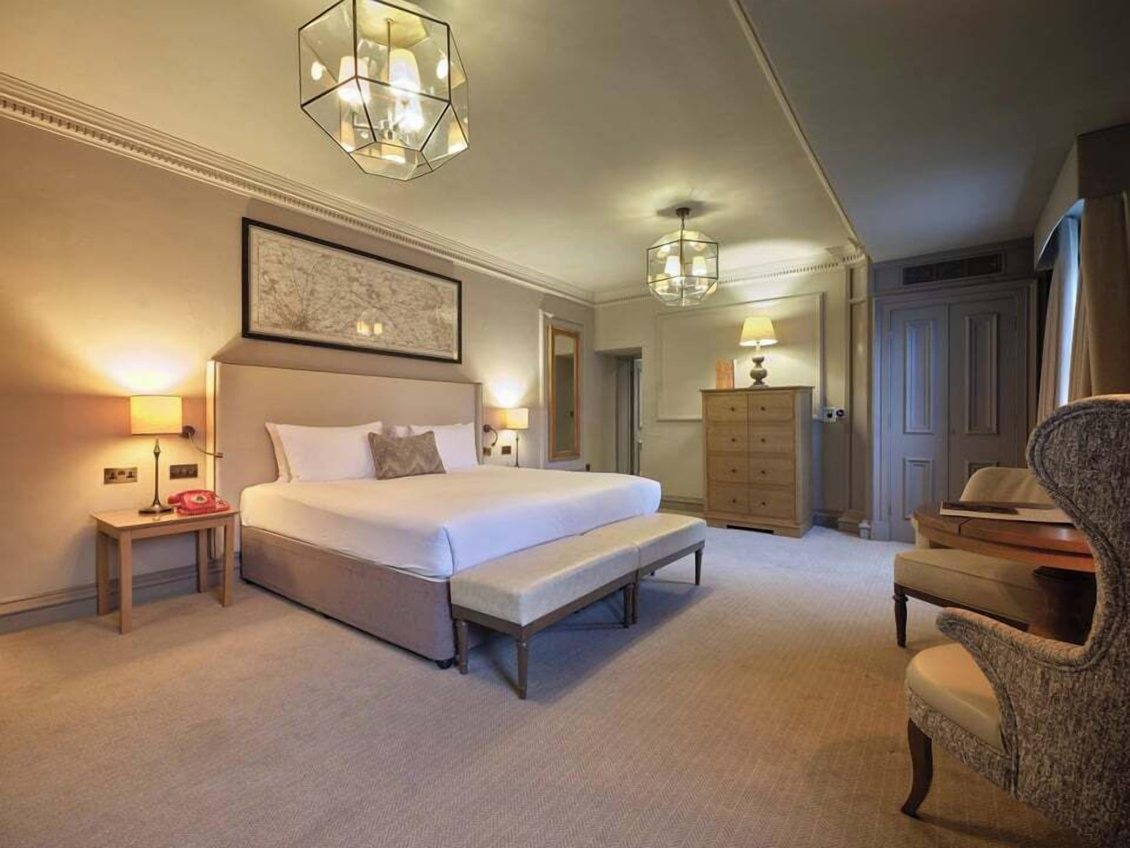 A hotel room with a large bed, bedside lamps, a desk, a chair, and a wardrobe.