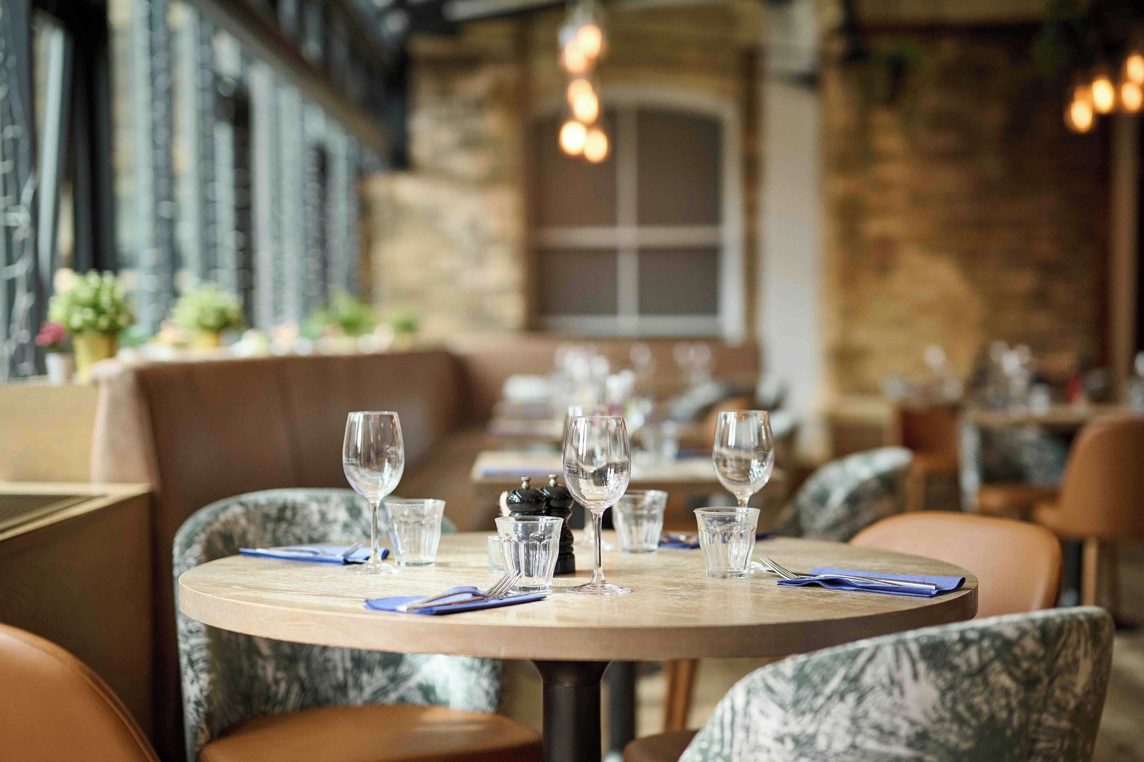 A restaurant with round tables, each set with wine glasses and cutlery.