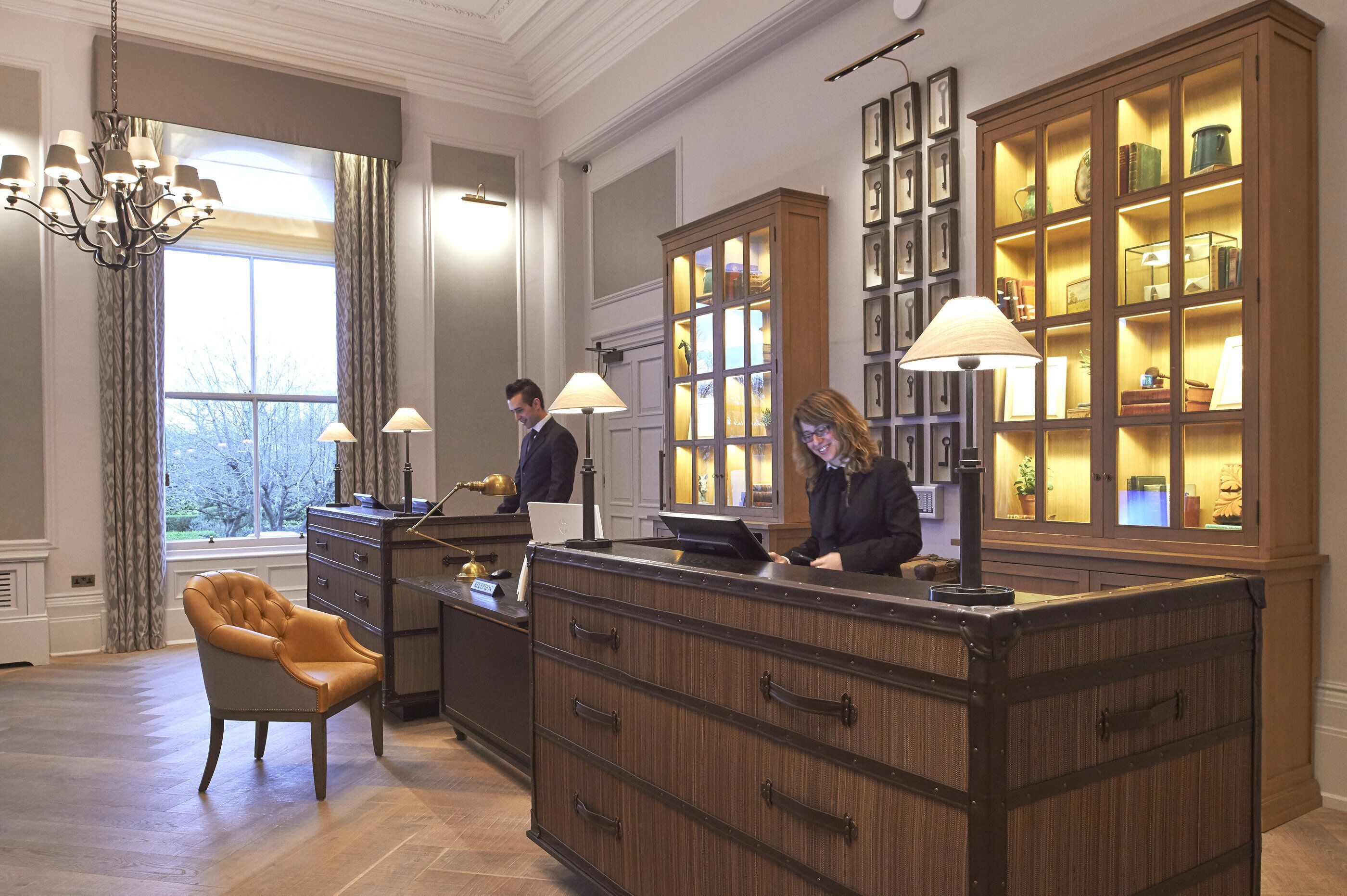 Un área de recepción con un escritorio de madera, un sillón de cuero y un gran aparador con puertas de vidrio que exhibe objetos.