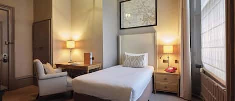 Una camera d'albergo con un letto grande, una scrivania, una sedia e un comodino con una lampada.