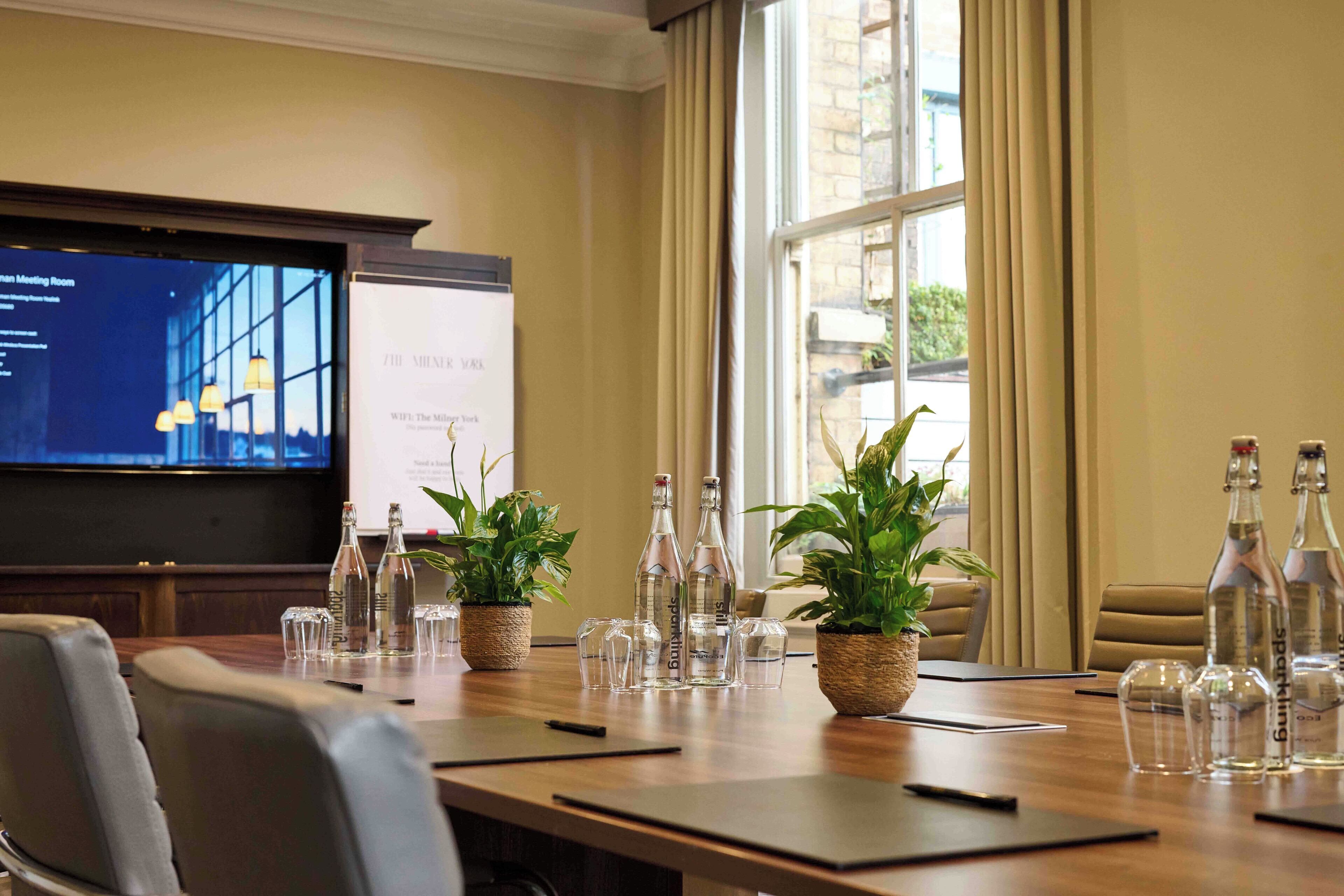 Un salón de conferencias con una pantalla grande, plantas en macetas y botellas de agua.
