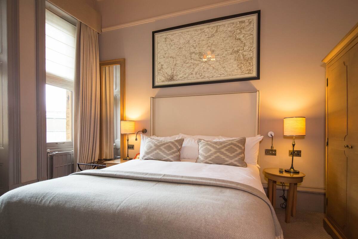 A hotel room with a large bed, two bedside lamps, a framed map on the wall, and a wooden wardrobe.
