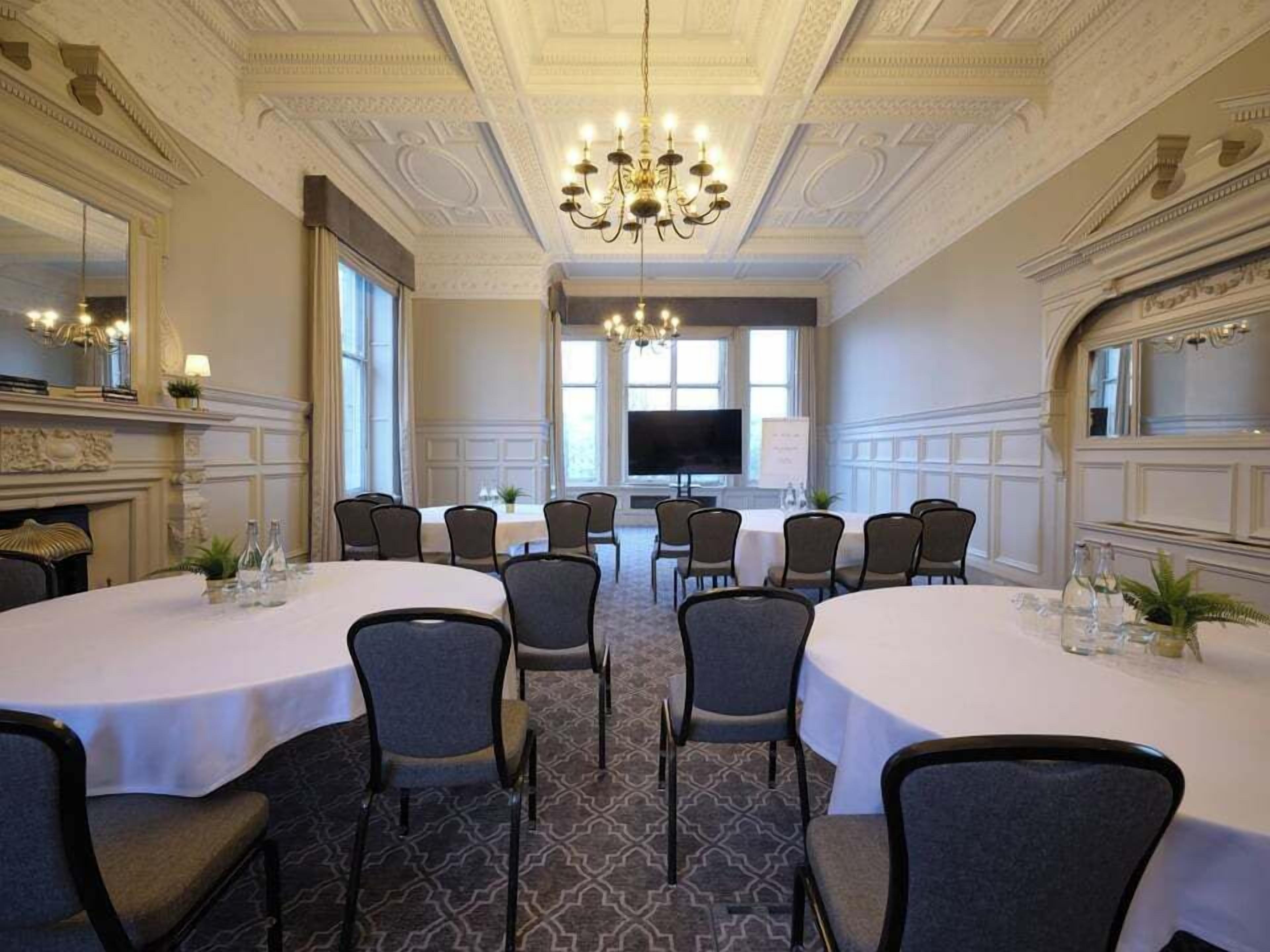 A conference room with a large table, chairs, a chandelier, and a television screen.