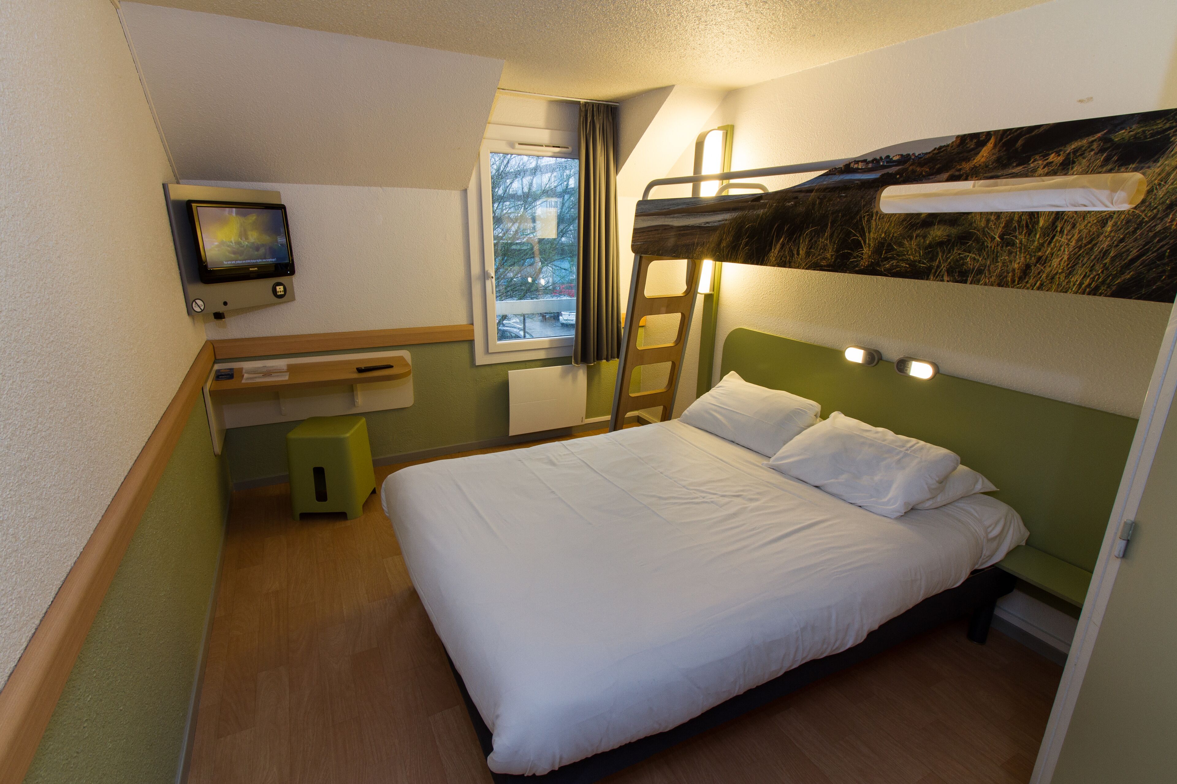 A bunk bed room with a television on the wall, a window, and a desk.